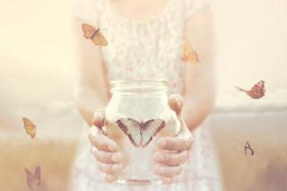 Žena drží otevřenou láhev s motýlem, v okolí létají další motýly.